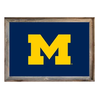 Framed Michigan Wolverines flag featuring maize block “M” on navy background, set in rustic light‑wood frame