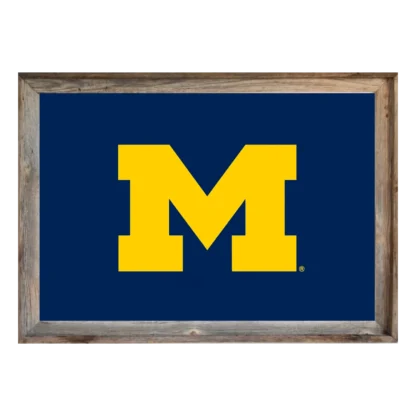 Framed Michigan Wolverines flag featuring maize block “M” on navy background, set in rustic light‑wood frame